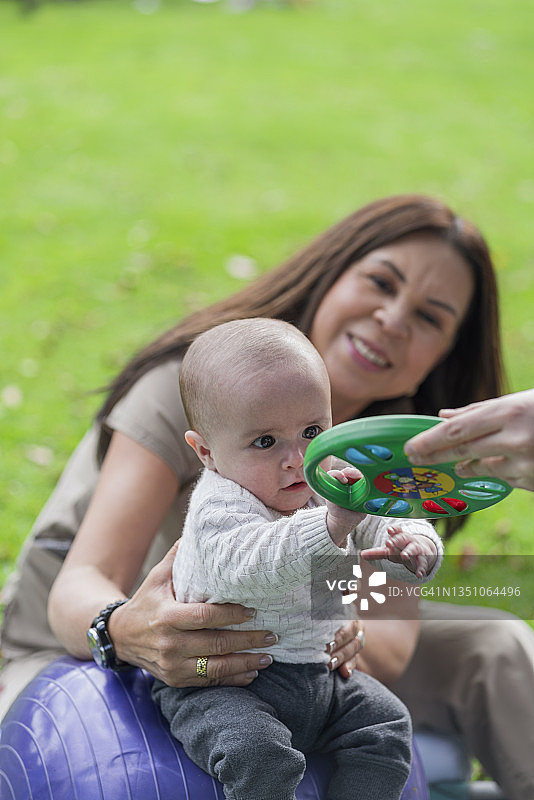 在公园里为婴儿做理疗，儿科医生和母亲鼓励婴儿做运动图片素材