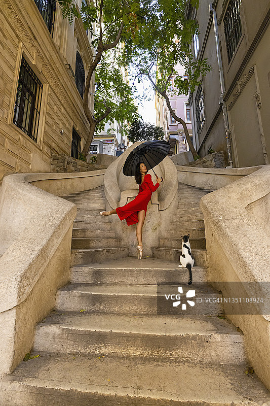在土耳其伊斯坦布尔卡蒙多楼梯上跳舞的芭蕾舞女演员和观看她的流浪猫图片素材