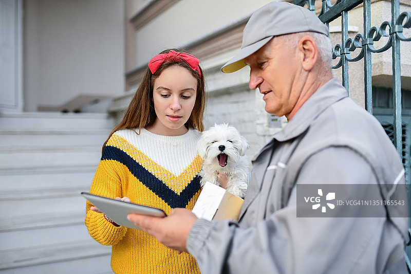 可爱的年轻女人为年长的邮递员签署电子收据图片素材