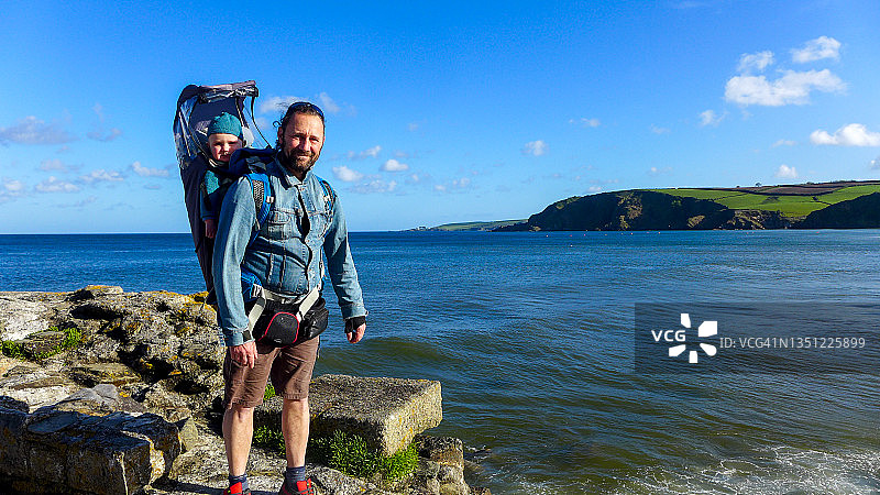 父亲和一岁大的男婴在英国康沃尔Pentewan的海岸线上徒步旅行图片素材