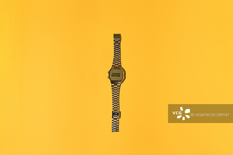 80年代的金色数字手表，黄色背景上的硬阴影。时间、复古、怀旧和80年代概念图片素材