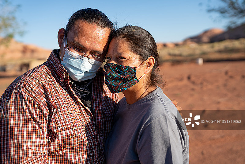 在亚利桑那州/犹他州边界的纪念碑谷部落公园中拥抱并戴着 Covid-19 冠状病毒口罩的年轻纳瓦霍夫妇图片素材