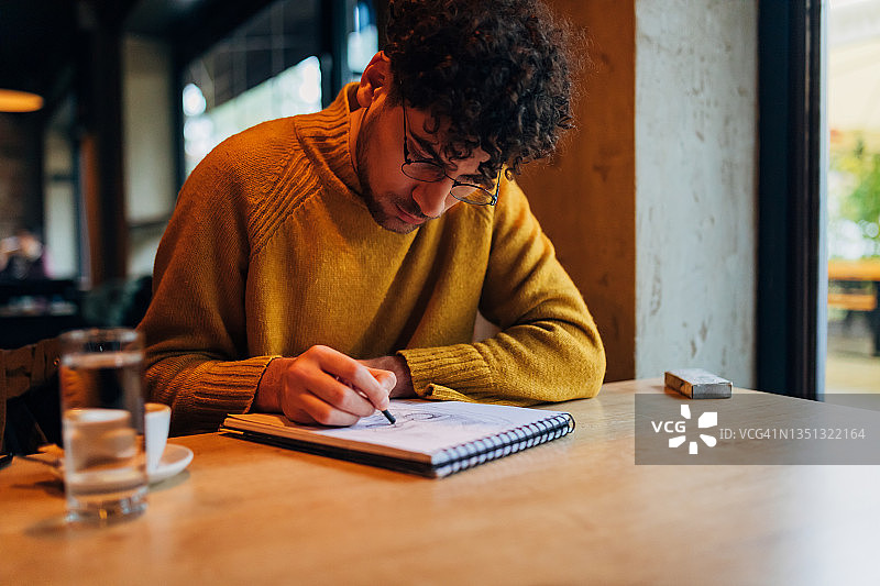 在自助餐厅喝浓缩咖啡时，一位才华横溢的年轻男人在笔记本上画草图图片素材