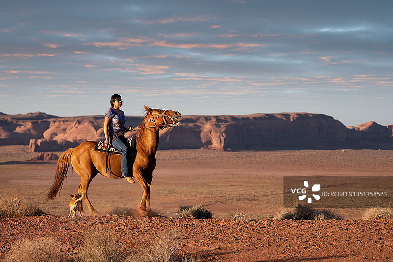 骑马的纳瓦霍族少女与狗：美国犹他州/亚利桑那州纪念碑谷部落公园图片素材