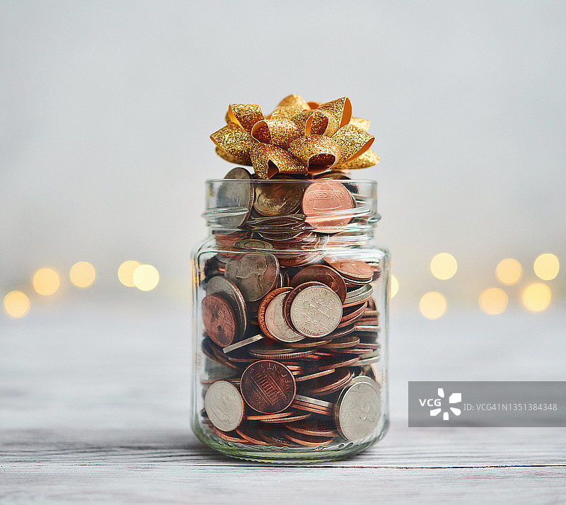 装满硬币的罐子，圣诞背景前的蝴蝶结和串灯图片素材