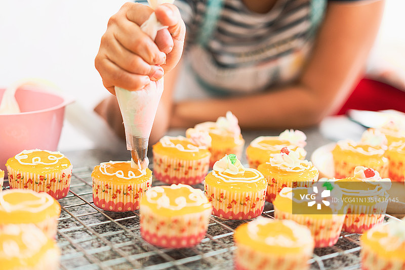年轻亚洲女人用裱花袋制作纸杯蛋糕图片素材