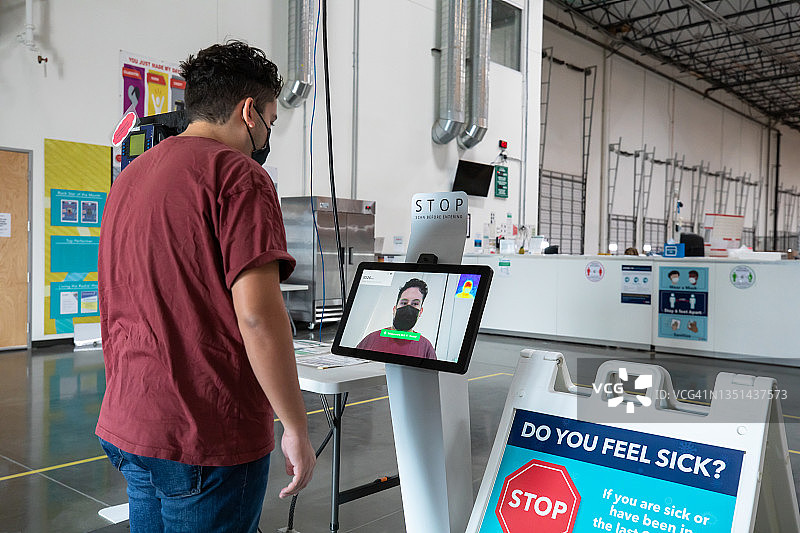 在物流中心入口使用测温仪的戴口罩男子图片素材