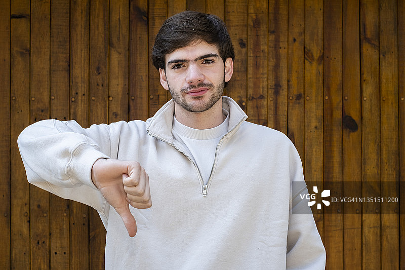 看着镜头并竖起大拇指向下的年轻拉丁裔男人图片素材