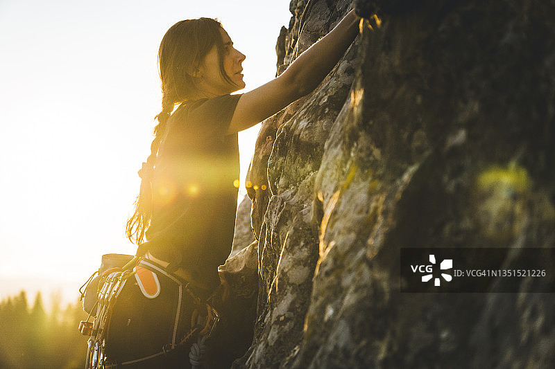 日出时，女子带头攀登岩石图片素材