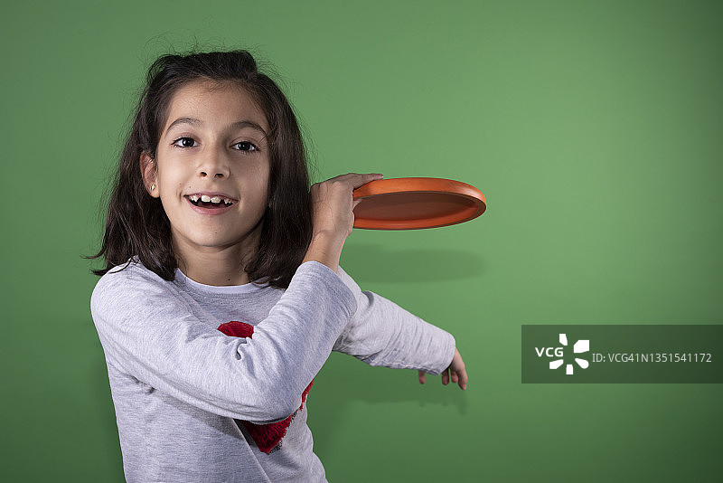 绿色背景下拿着飞盘的快乐八岁女孩看着镜头图片素材