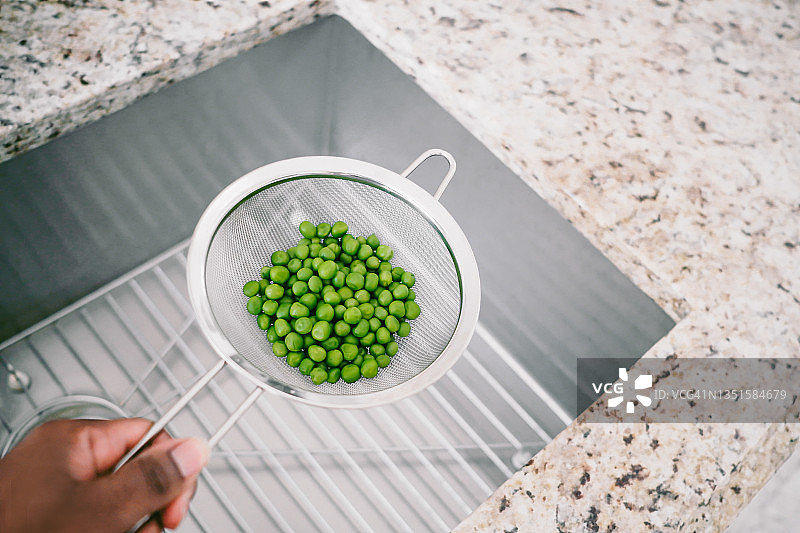 在厨房水槽上过滤青豌豆的女人图片素材