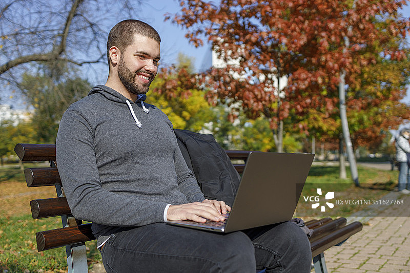男人在公园里使用笔记本电脑，面带微笑图片素材