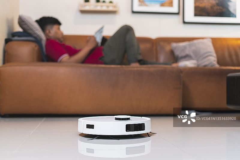 男人在沙发上看电视，扫地机器人打扫房间图片素材