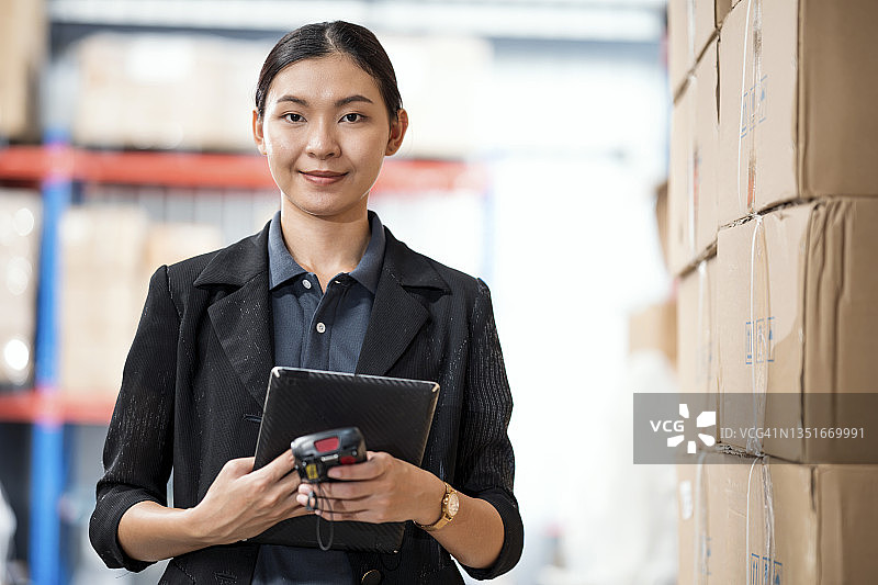 库存预测与计划：亚洲女性仓库经理手持库存清单和条形码扫描器在现代化仓库中图片素材