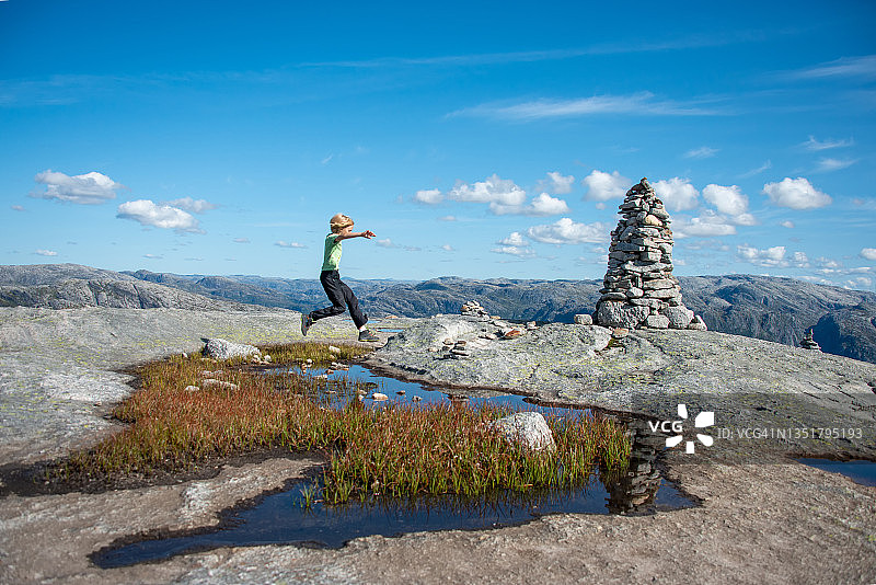 男孩在挪威奇迹石徒步小径上攀爬跳跃图片素材