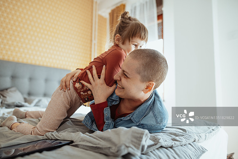 身患癌症的母亲和女儿玩耍，女儿在床上跳跃图片素材