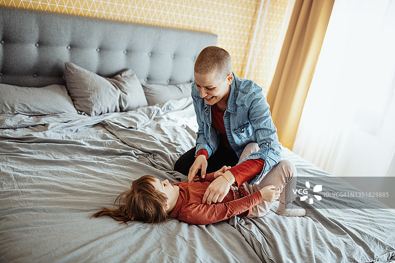 身患癌症的母亲和女儿玩耍，女儿在床上跳跃图片素材