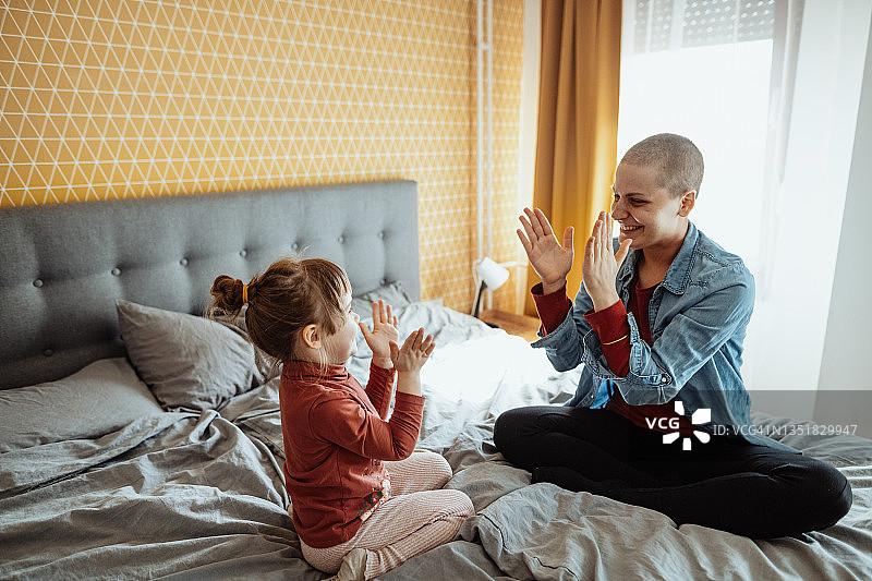 身患癌症的母亲和女儿玩耍，女儿在床上跳跃图片素材