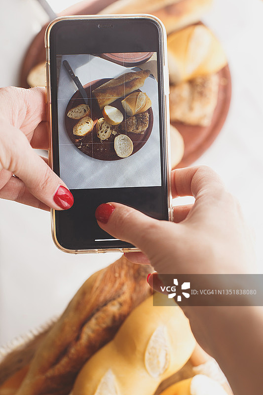 女士的双手在手机上为博客拍摄食物面包照片图片素材