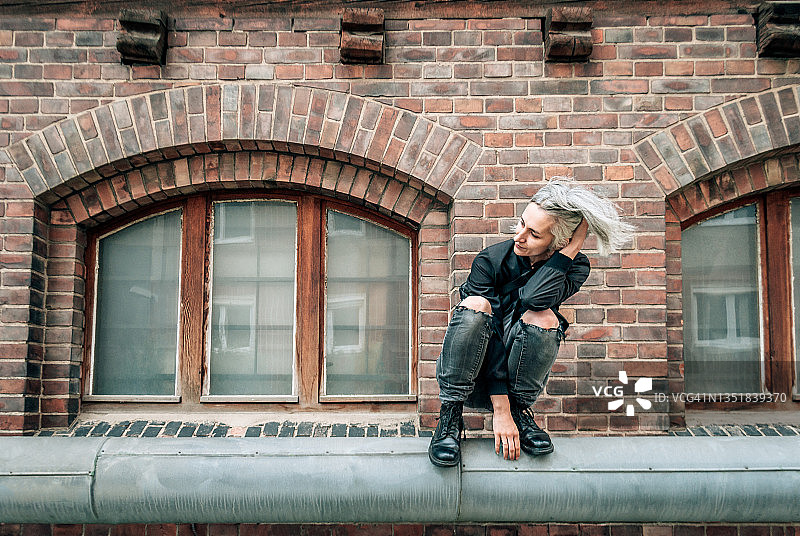 穿破洞牛仔裤的女人蹲在废弃建筑旁的管道上图片素材
