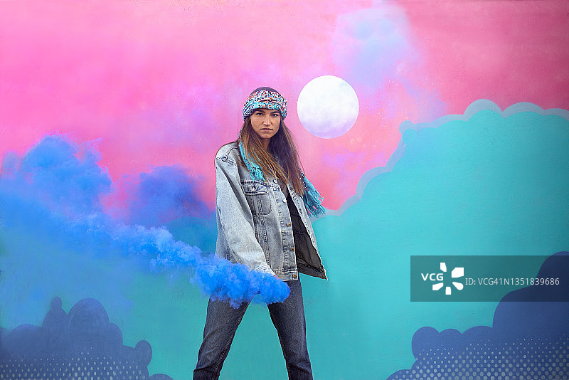 手持烟雾弹的时尚女孩，背景是彩色墙绘艺术图片素材