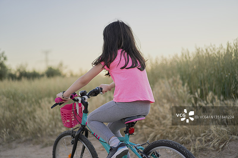 快乐的女孩在日落时分骑自行车行驶在田野的道路上图片素材