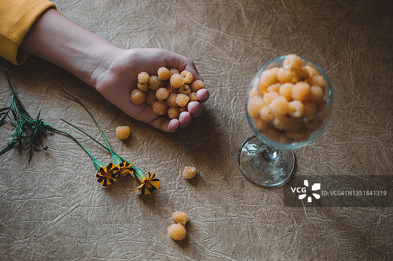 玻璃杯中和手中的黄色覆盆子与万寿菊图片素材