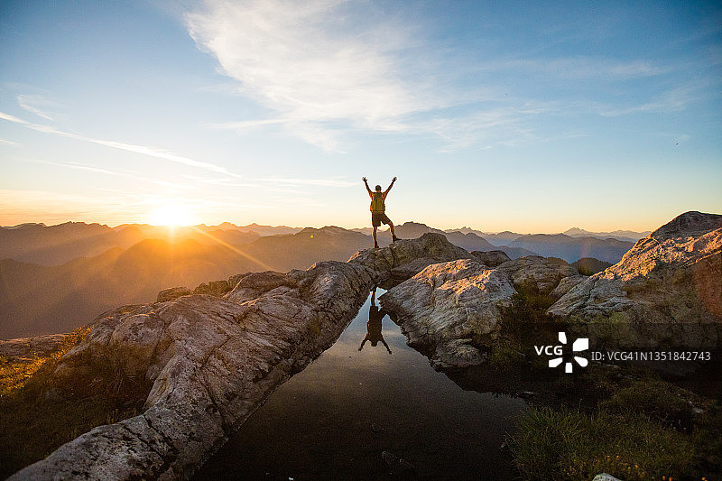 徒步者站在山顶，伸手向天空，象征成功图片素材