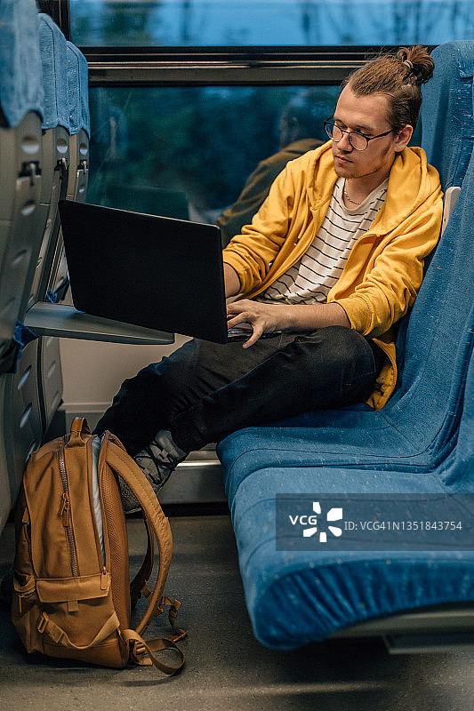 戴眼镜的青少年男子在火车上用笔记本电脑旅行图片素材