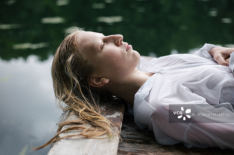 穿着白色衬衫的金发少女躺在池塘边，头发湿漉漉的图片素材
