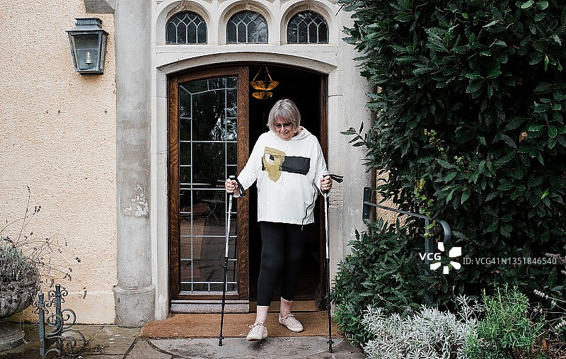 拄着拐杖穿过乡村住宅门的女人图片素材