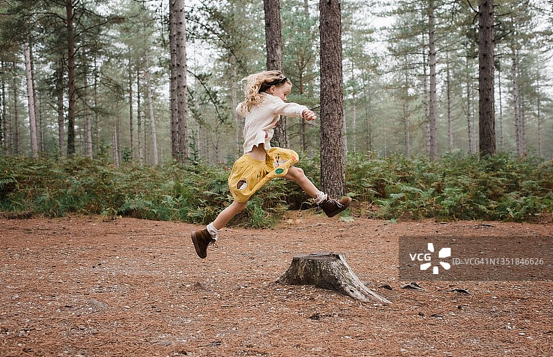 秋天，在森林里跳过树桩的女孩图片素材