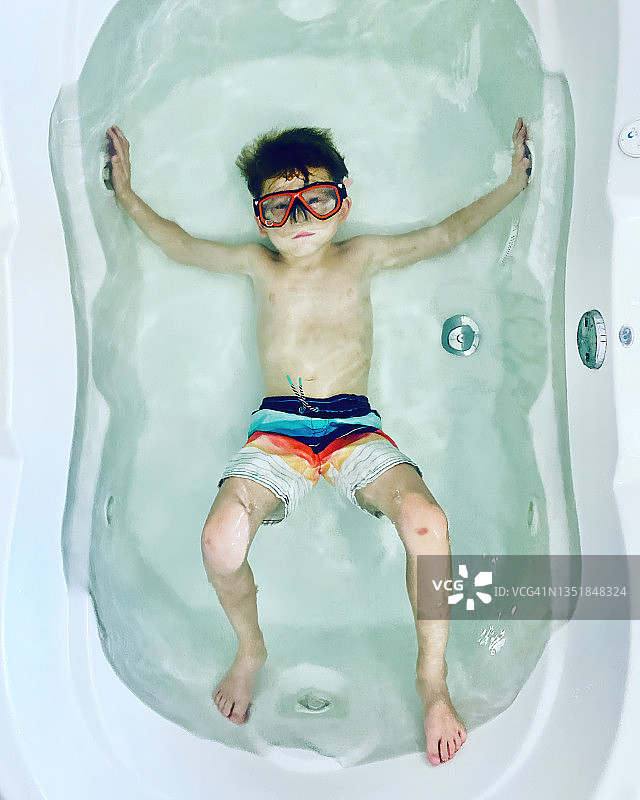 穿着泳裤和潜水面罩的忧郁男孩在大浴缸里图片素材