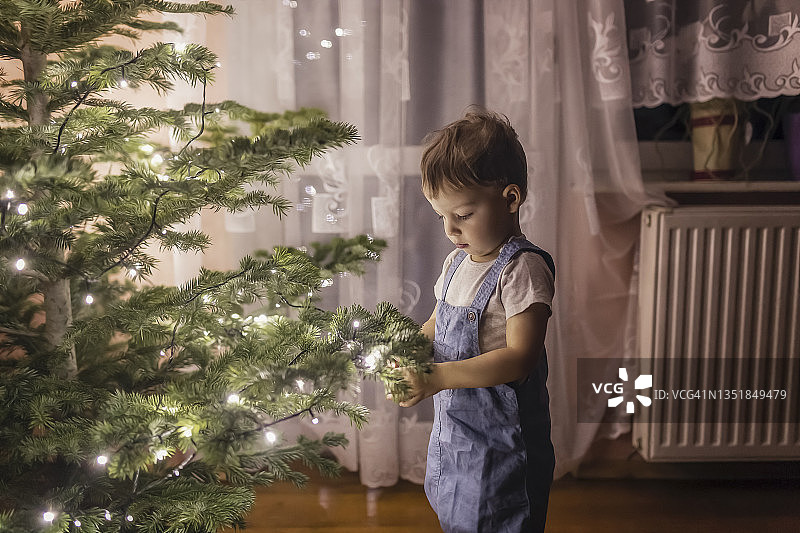 穿蓝色工装裤的幼儿装饰圣诞树图片素材