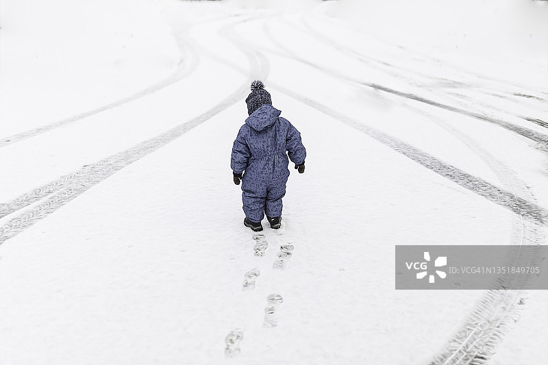 穿着蓝色连体衣在雪地里行走的小男孩图片素材