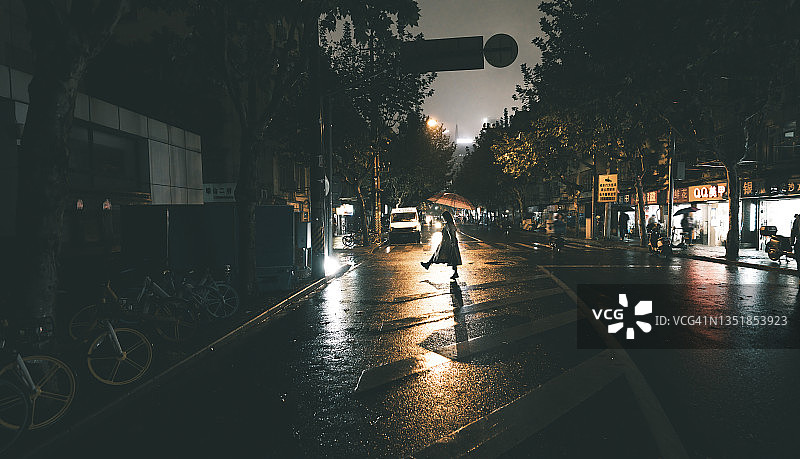 一位年轻的亚洲女士在上海的雨夜里撑伞行走图片素材