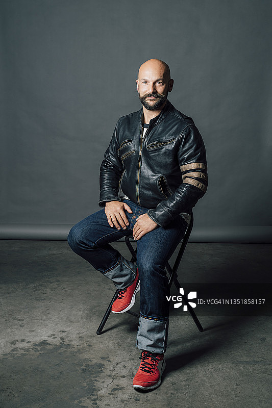 中年男人坐在灰色背景前的椅子上图片素材