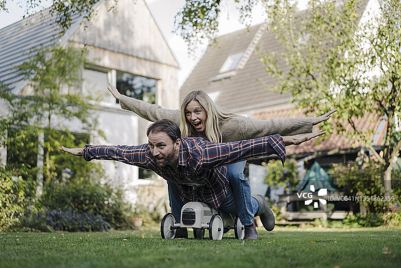 在花园里玩具车上假装飞翔的欢笑情侣图片素材