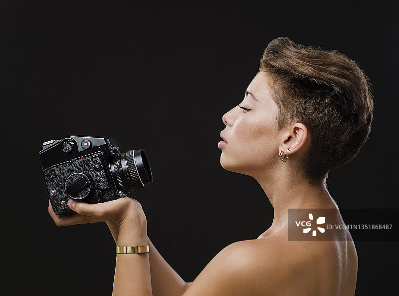 年轻女子在黑色背景前使用中画幅相机拍照图片素材