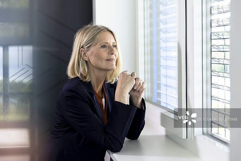 靠在窗台上沉思的金发女商人图片素材