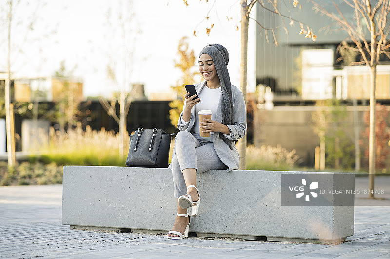 笑容满面的职业女性坐在人行道长椅上使用智能手机图片素材