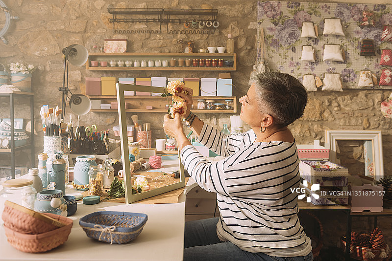 女人坐在工作台旁，用鲜花装饰相框图片素材