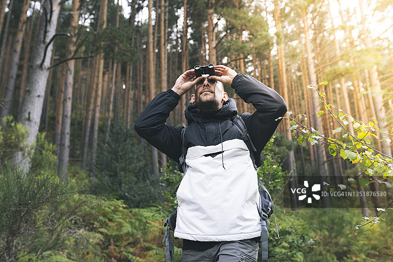 在森林中用双筒望远镜观察的男性游客图片素材