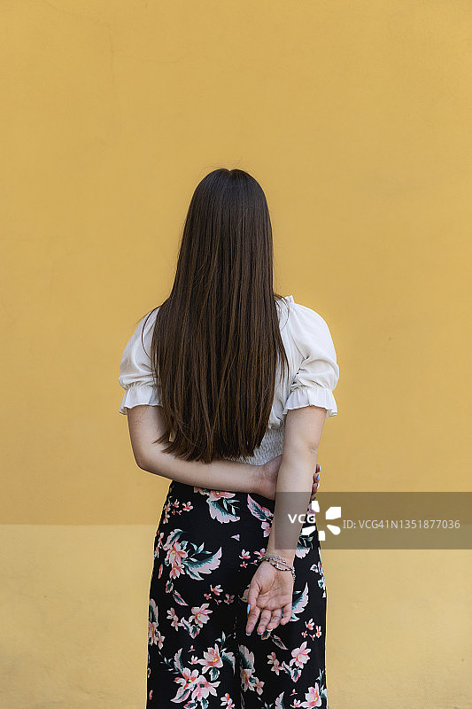 站在黄色背景前，双手背后的少女图片素材