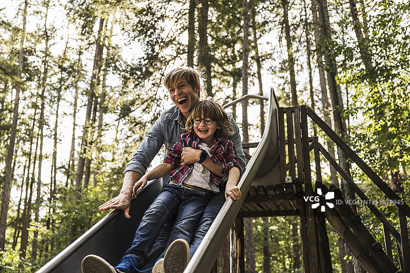 快乐的儿子和父亲在森林里的滑梯上玩耍图片素材