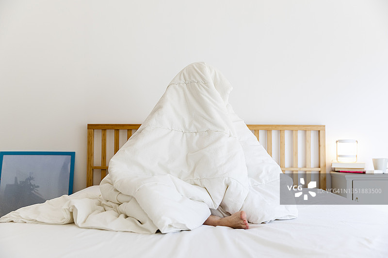 年轻女人裹着白色毯子坐在家里的床上图片素材