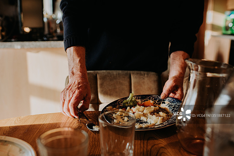 一名男子从木桌上端起一盘剩菜图片素材