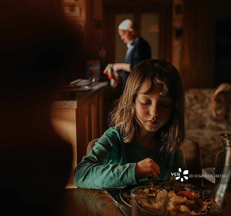 一个年轻女孩坐在厨房的桌子旁吃晚餐，场景宁静而平静图片素材