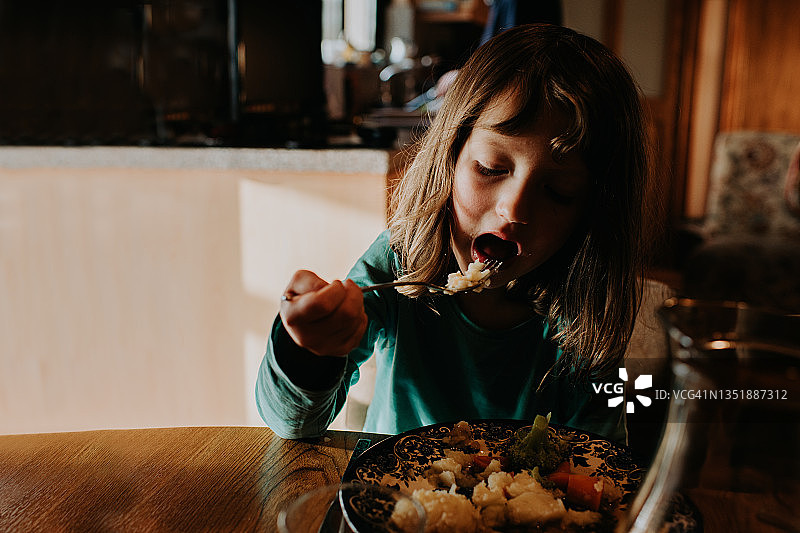 一个年轻女孩坐在厨房的桌子旁吃晚餐，场景宁静而平静图片素材