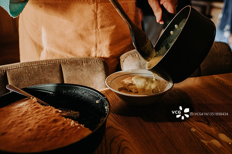 一名妇女将蛋奶沙司从平底锅倒到新鲜的海绵布丁上图片素材